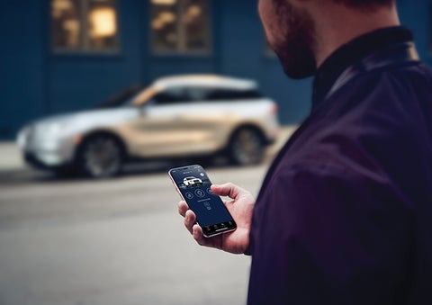 A person is shown interacting with a smartphone to connect to a Lincoln vehicle across the street. | John Vance Auto Group in Guthrie OK